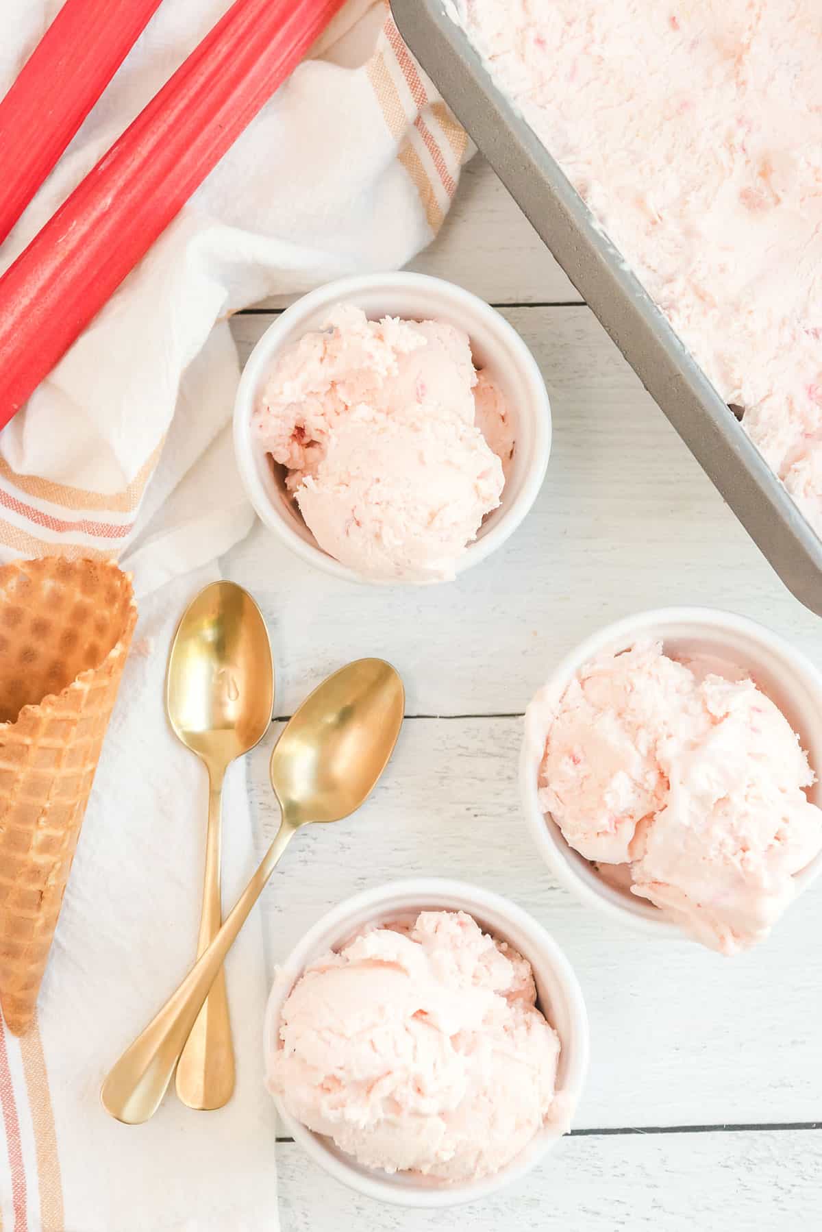 no churn rhubarb ice cream scooped in small white bowls with gold spoons