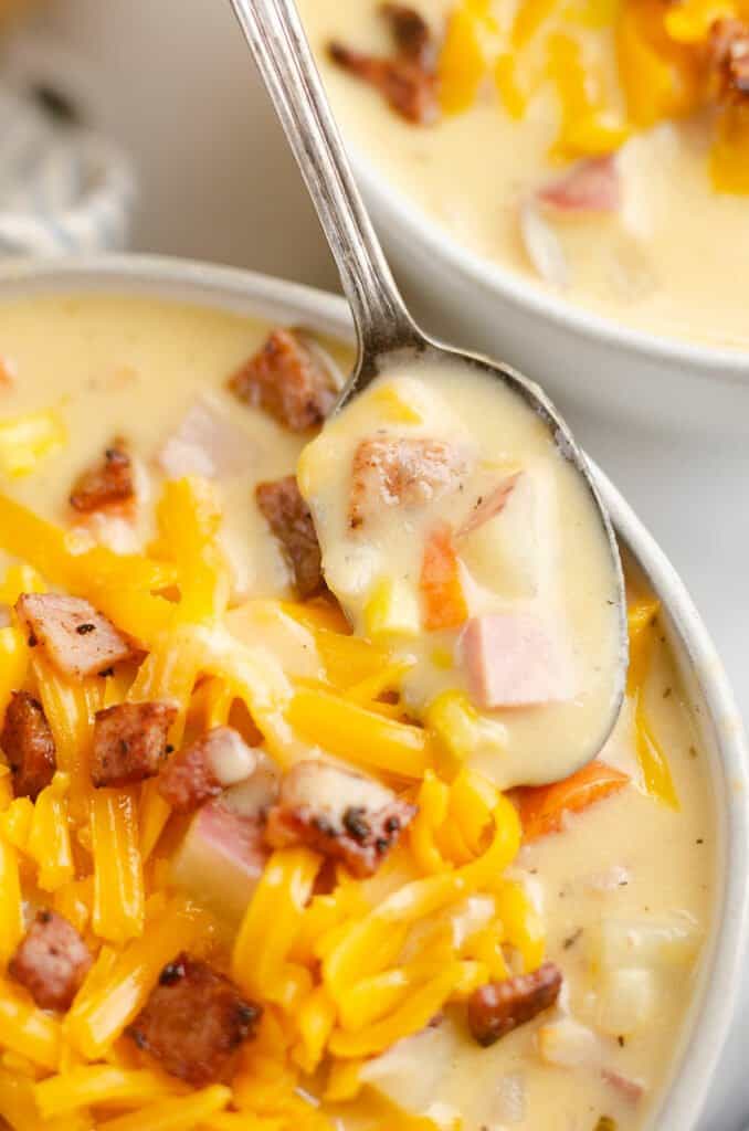 spoonful of creamy ham and potato soup resting on bowl topped with cheese