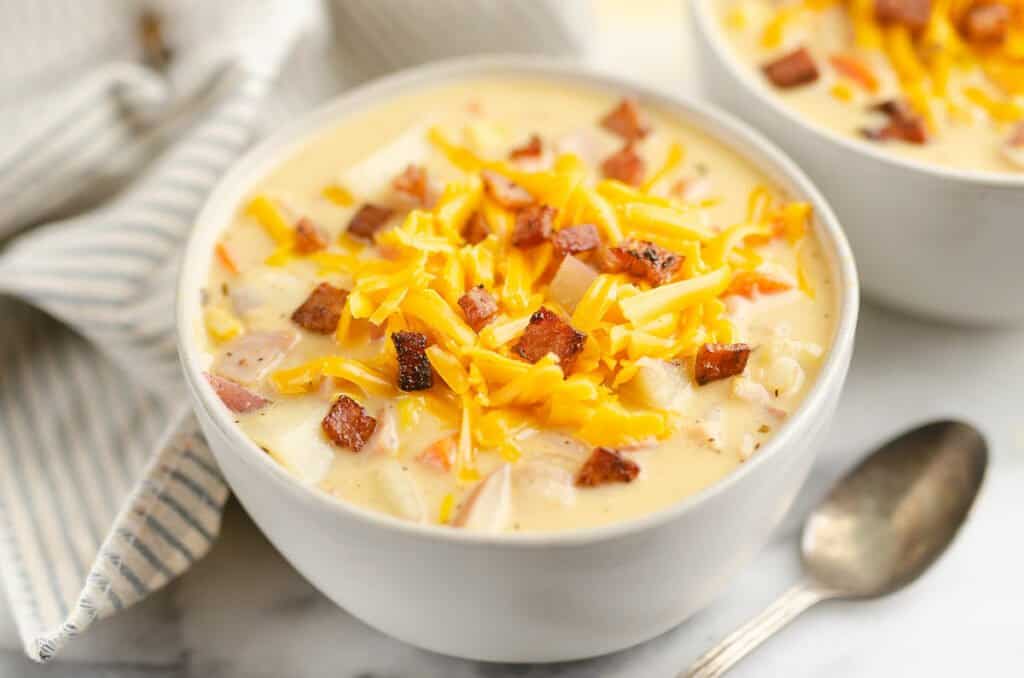 creamy ham and potato soup in white bowl topped with cheddar cheese and crispy ham