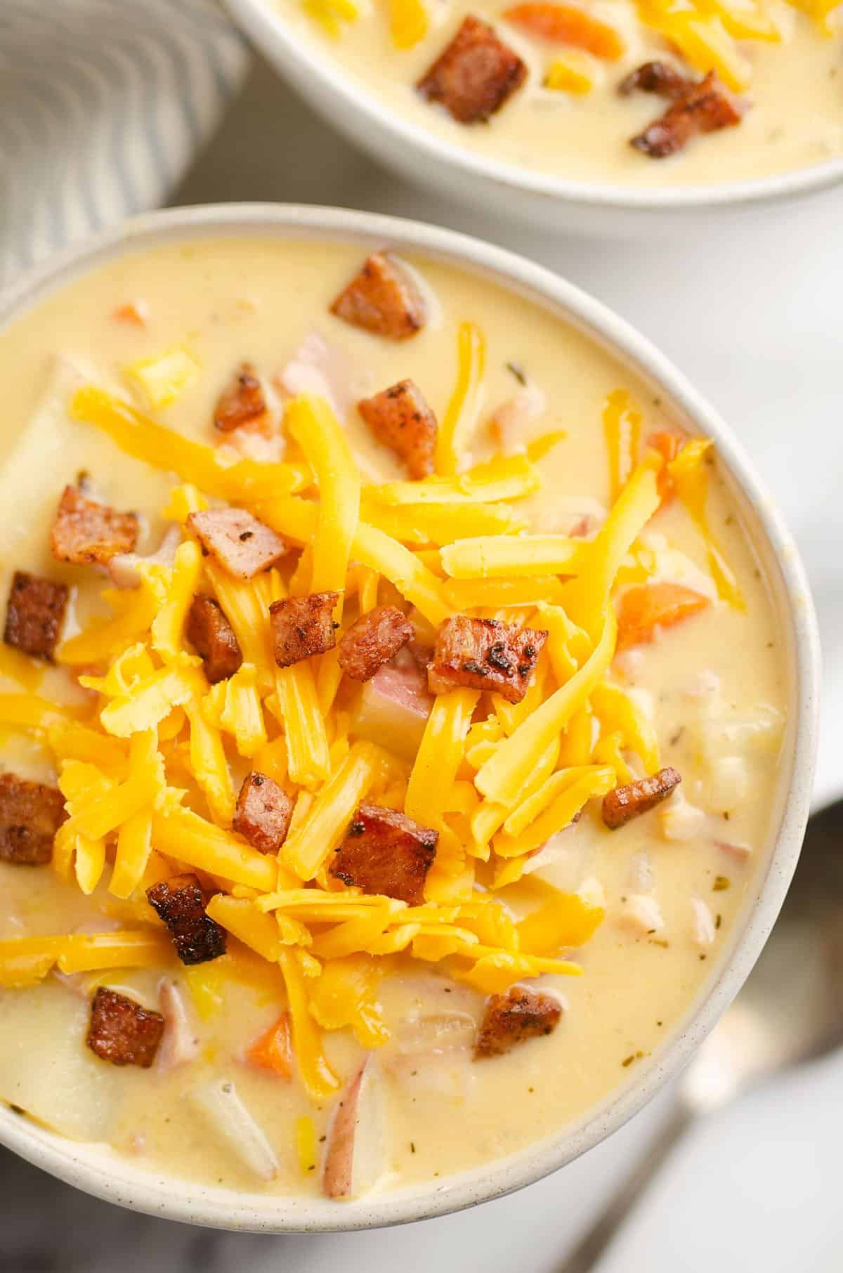 creamy ham and potato soup in white bowl topped with cheddar cheese and crispy ham