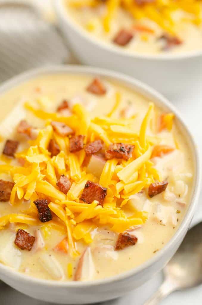 creamy ham and potato soup in white bowl topped with cheddar cheese and crispy ham