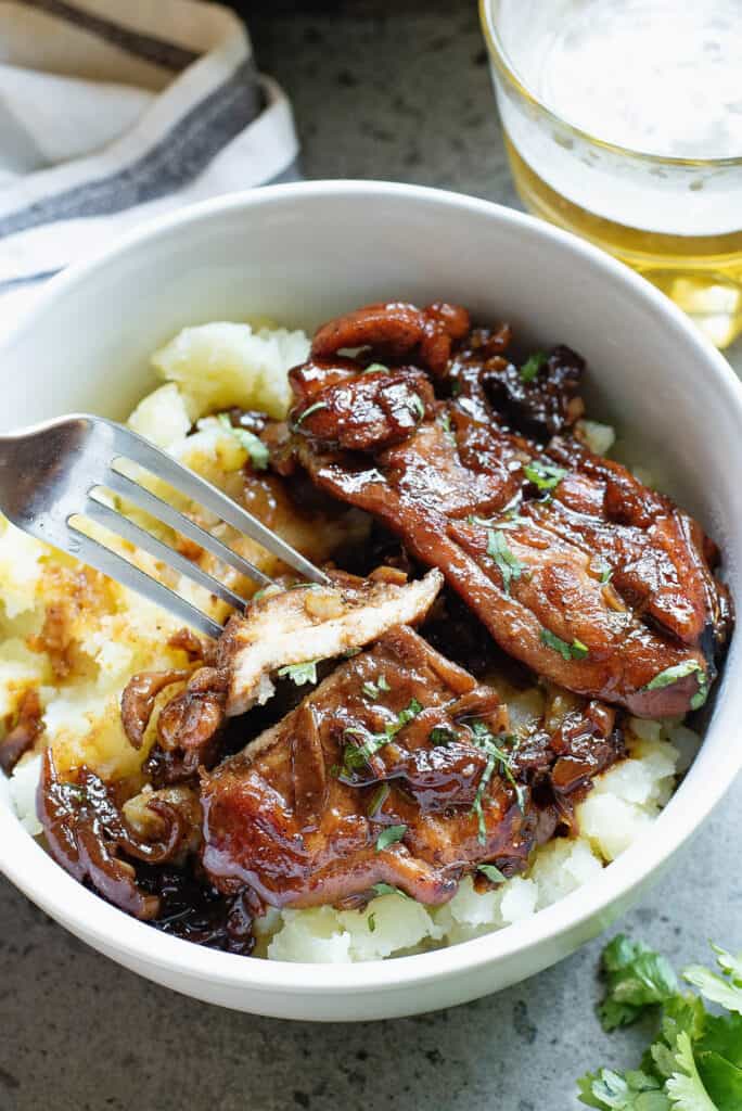 honey beer chicken thighs served over mashed potatoes in bowl and piece on fork
