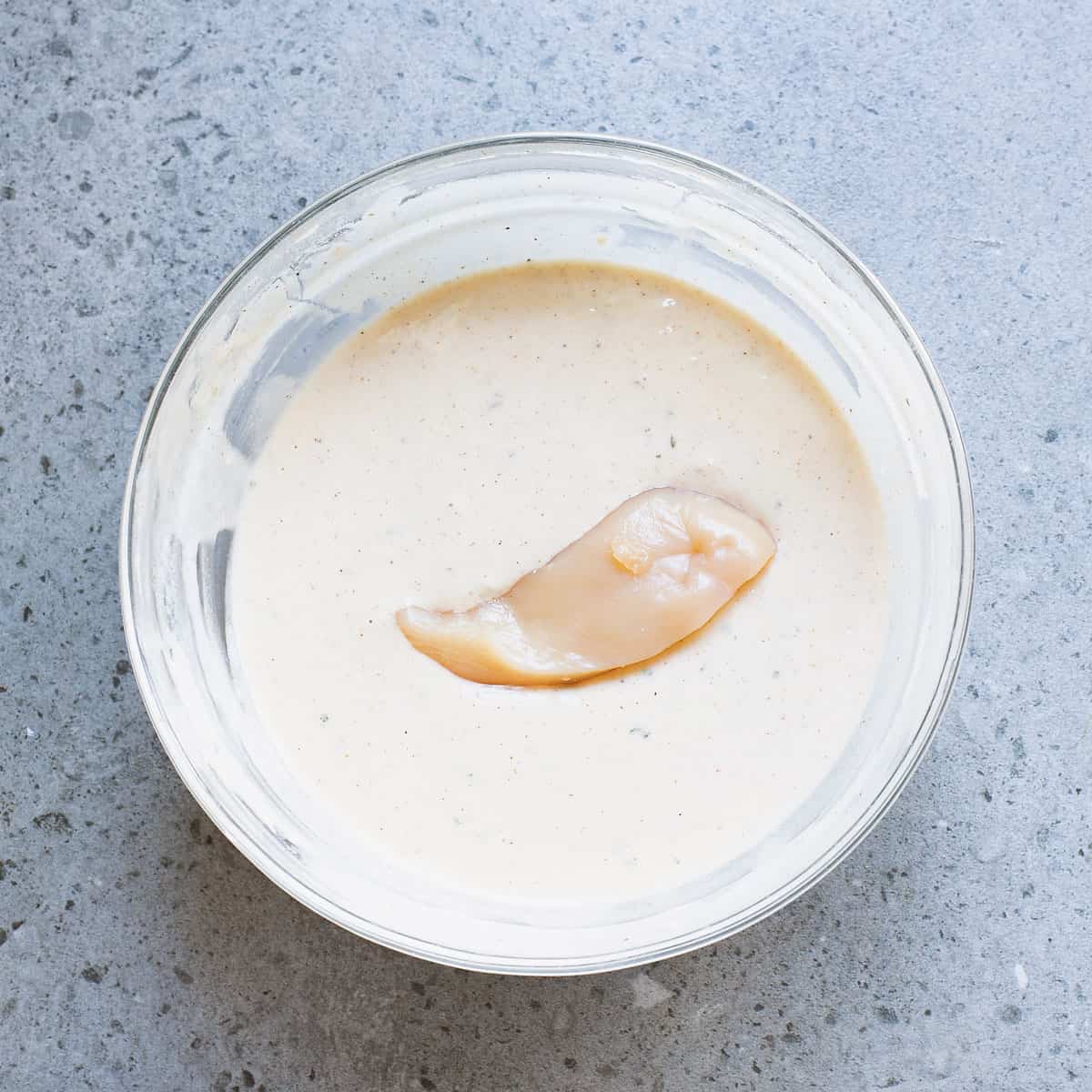 glass bowl of beer batter with chicken tender in it