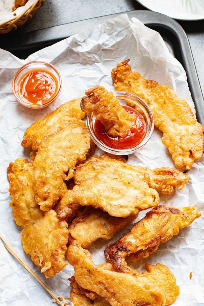 beer battered chicken tenders on parchment with dipping sauces
