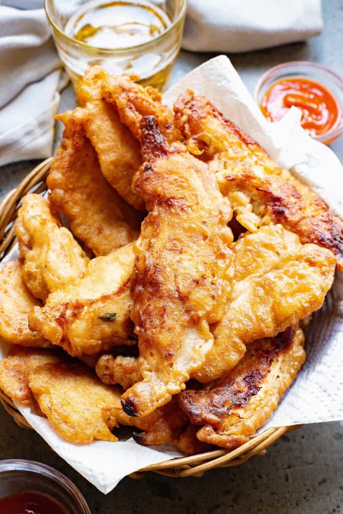 beer battered chicken tenders in lined basket with cup of beer and ketchup