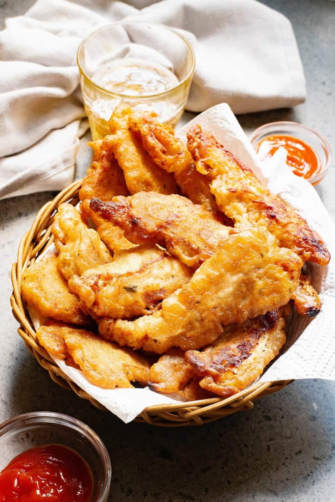 beer battered chicken tenders in basket on table with dipping sauces and glass of beer