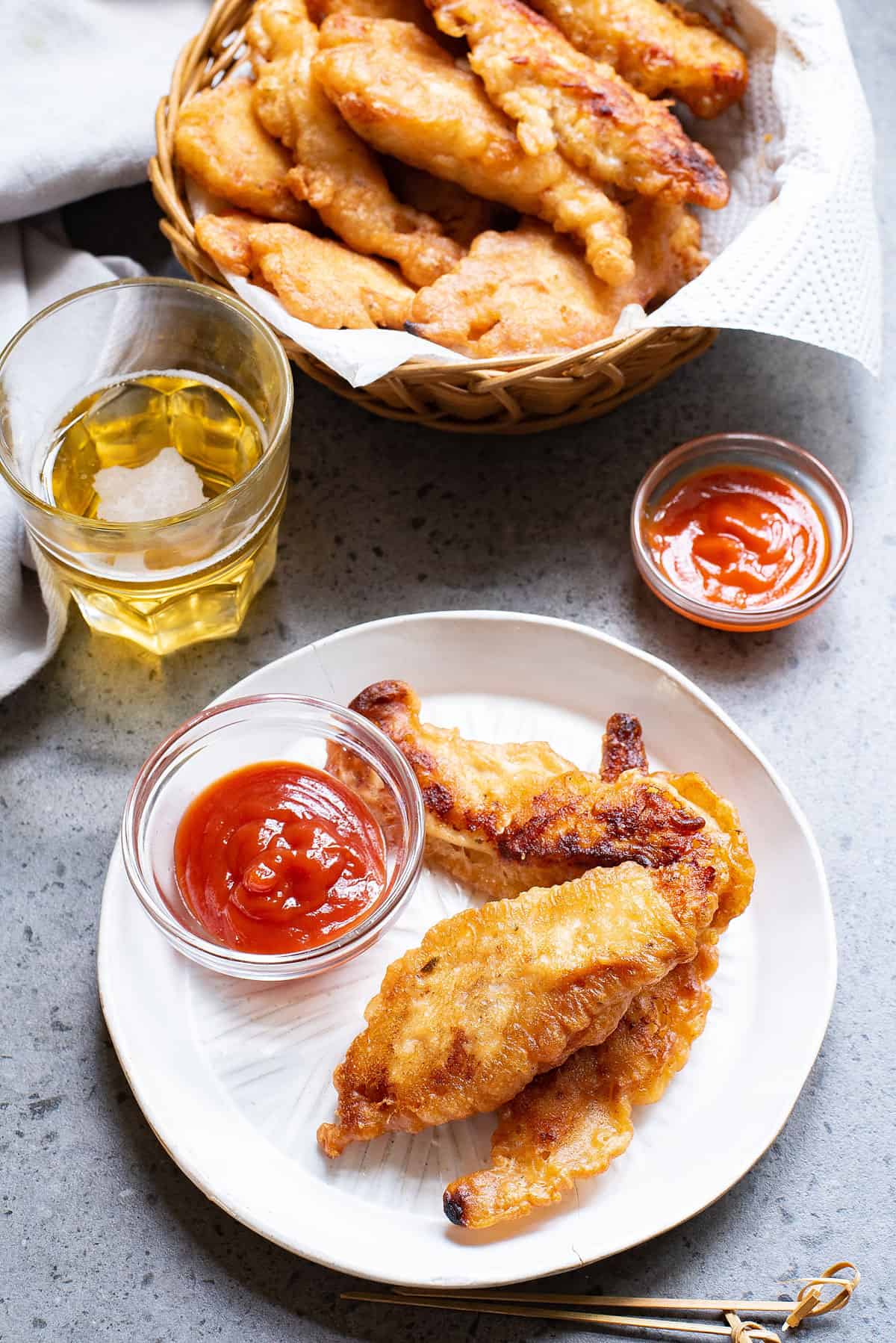 beer battered chicken tenders served on white plate with cup of ketchup and glass of beer