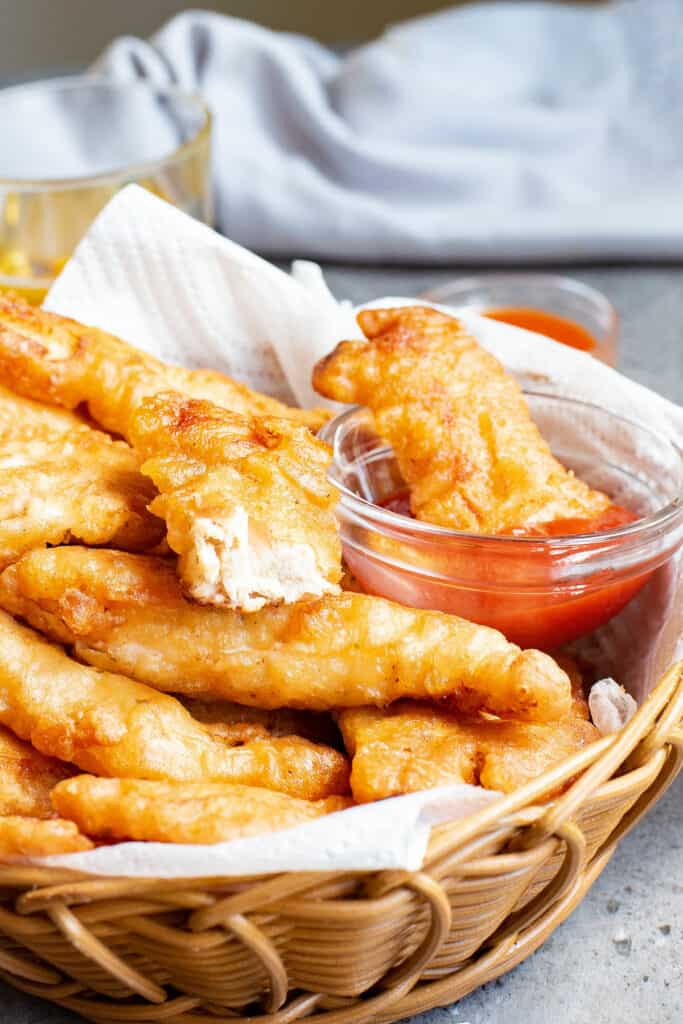 beer battered chicken tenders in basket, dipped in ketchup