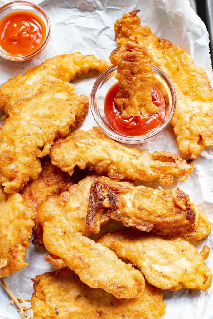 beer battered chicken tenders on parchment lined baking sheet and dunked in ketchup