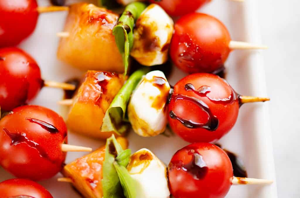peach caprese bites on toothpicks on white platter with balsamic drizzle