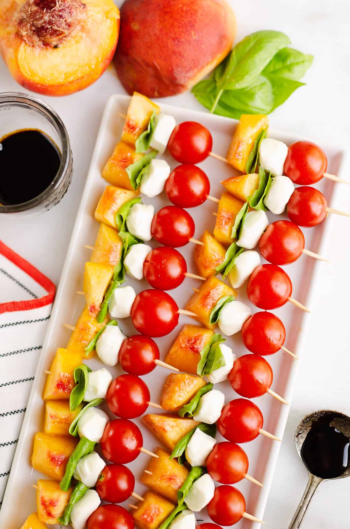 white serving platter filled with peach, tomato and mozzarella skewers in a line