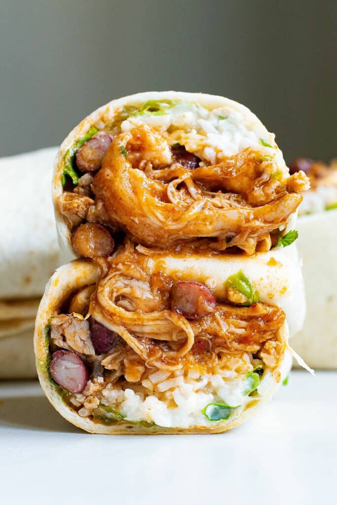 sliced pulled pork and rice burrito in half stacked on table