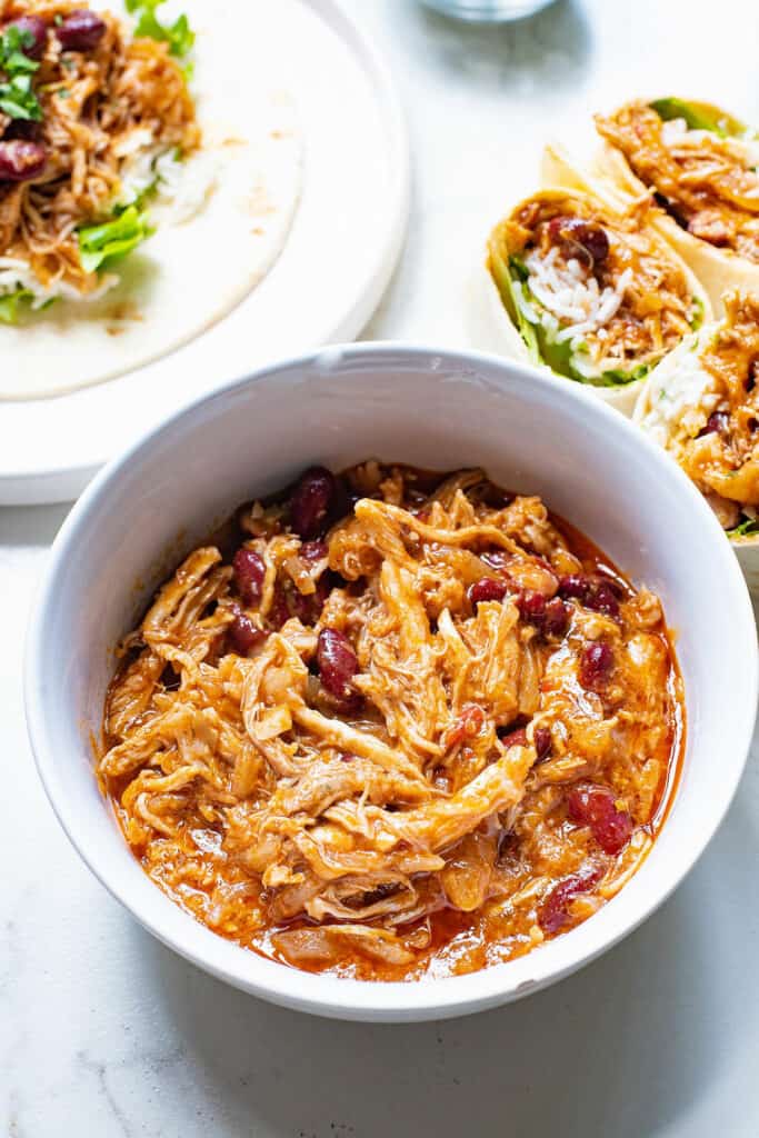 bowl of pulled pork with red kidney beans on table with burritos