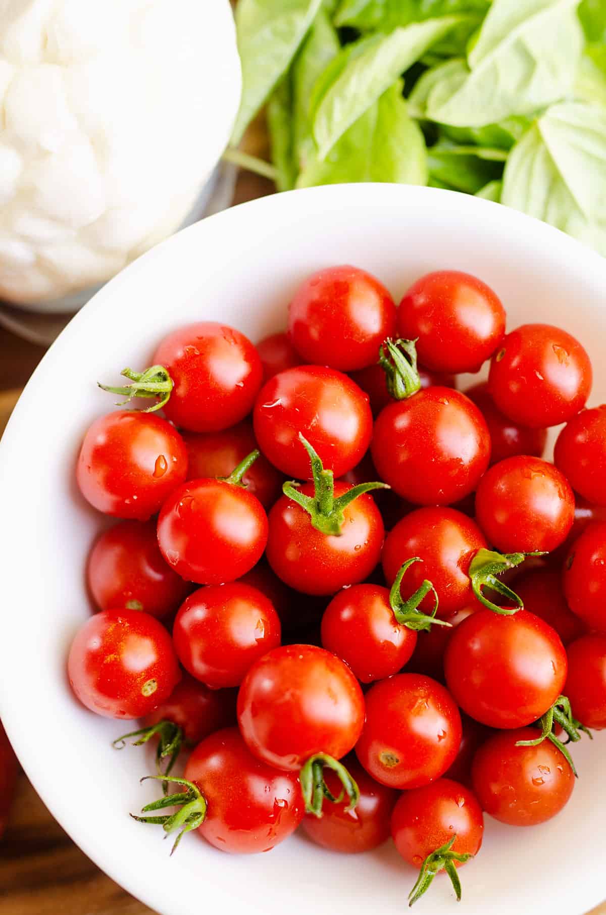 fresh cherry tomatoes in bowl next to basil and cheese