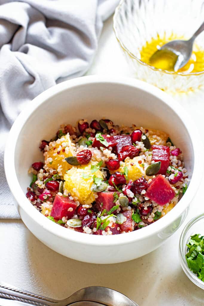 beet orange and pomegranate quiona salad in bowl next to vinaigrette and parsley