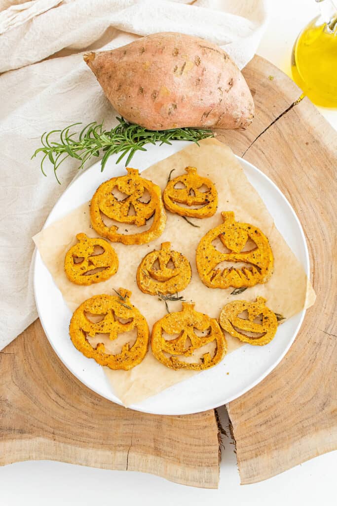 jack o lantern roasted sweet potatoes arranged on lined plate with large sweet potato and rosemary