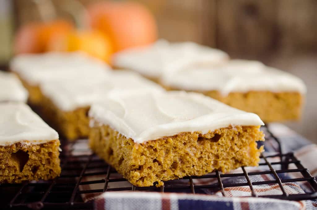 pumpkin cake bars frosted with cream cheese frosting on cooling rack
