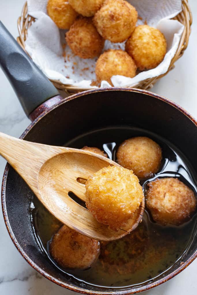 mashed potato ball fried in pot of oil with wooden spoon