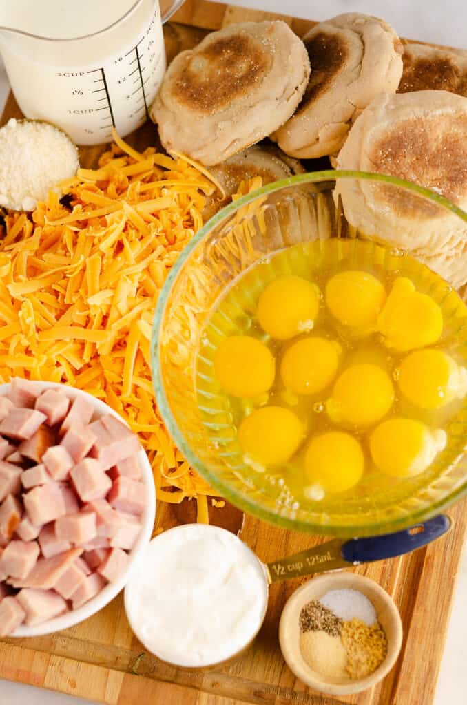 eggs, cheese, greek yogurt, spices, english muffins and milk on cutting board