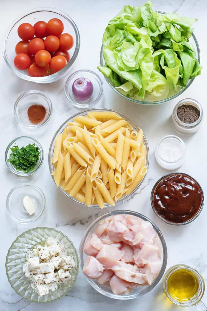 bowls of lettuce, tomatoes, shallot, pasta, fetta and chicken on table