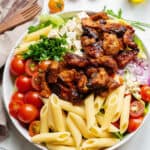 large salad bowl with bbq chicken, pasta, tomatoes and herbs