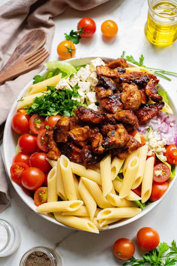 large salad bowl with bbq chicken, pasta, tomatoes and herbs