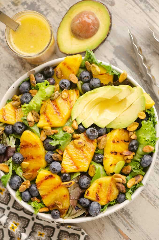 grilled pineapple and blueberry salad in bowl on table with avocado