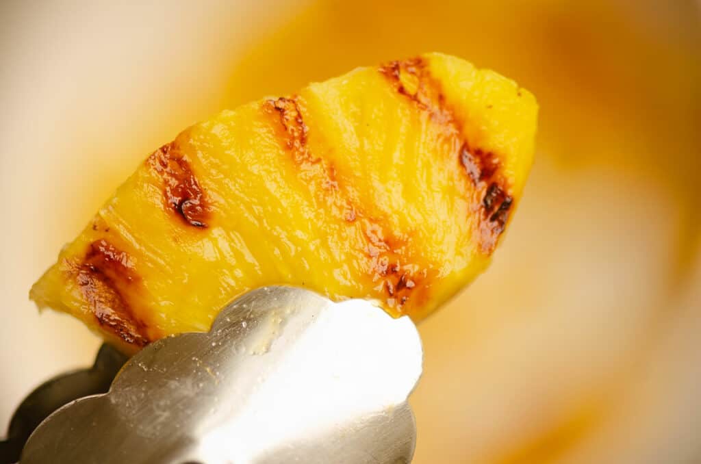 grilled pineapple in kitchen tongs