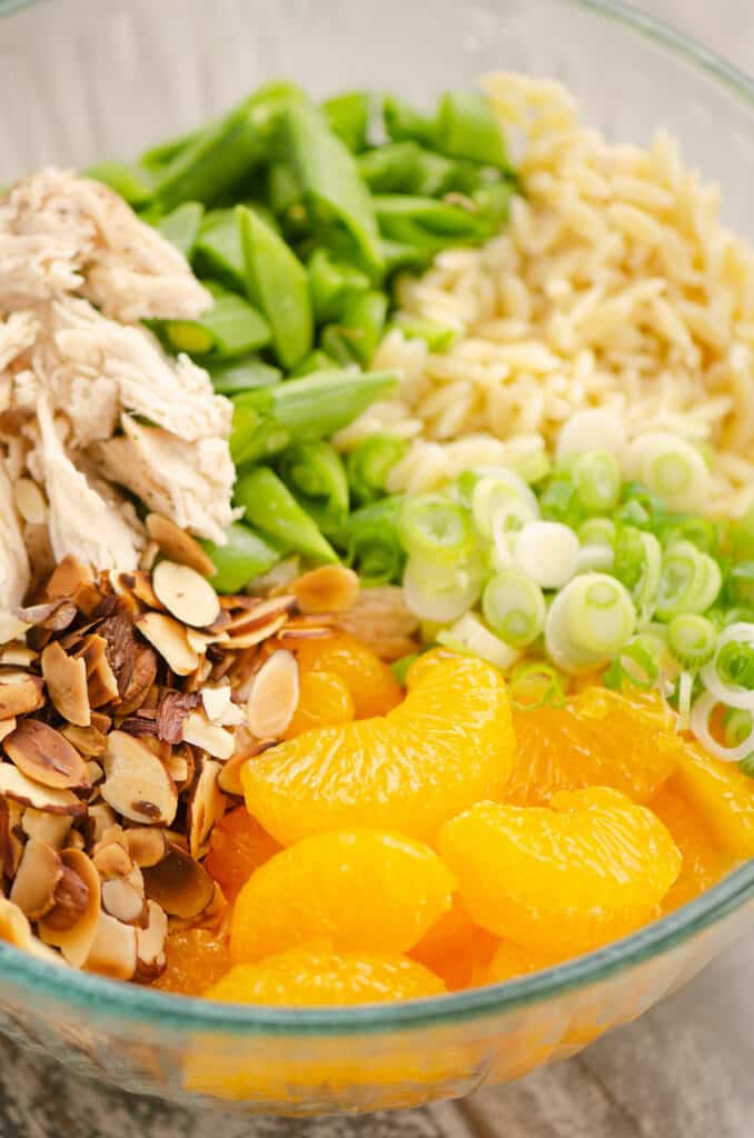 orzo pasta, oranges, onions, almonds and chicken in bowl