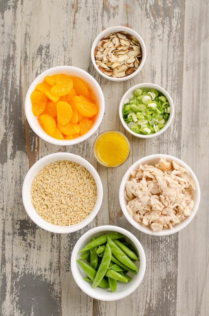 orzo pasta, oranges, onions, almonds and chicken in bowls on table