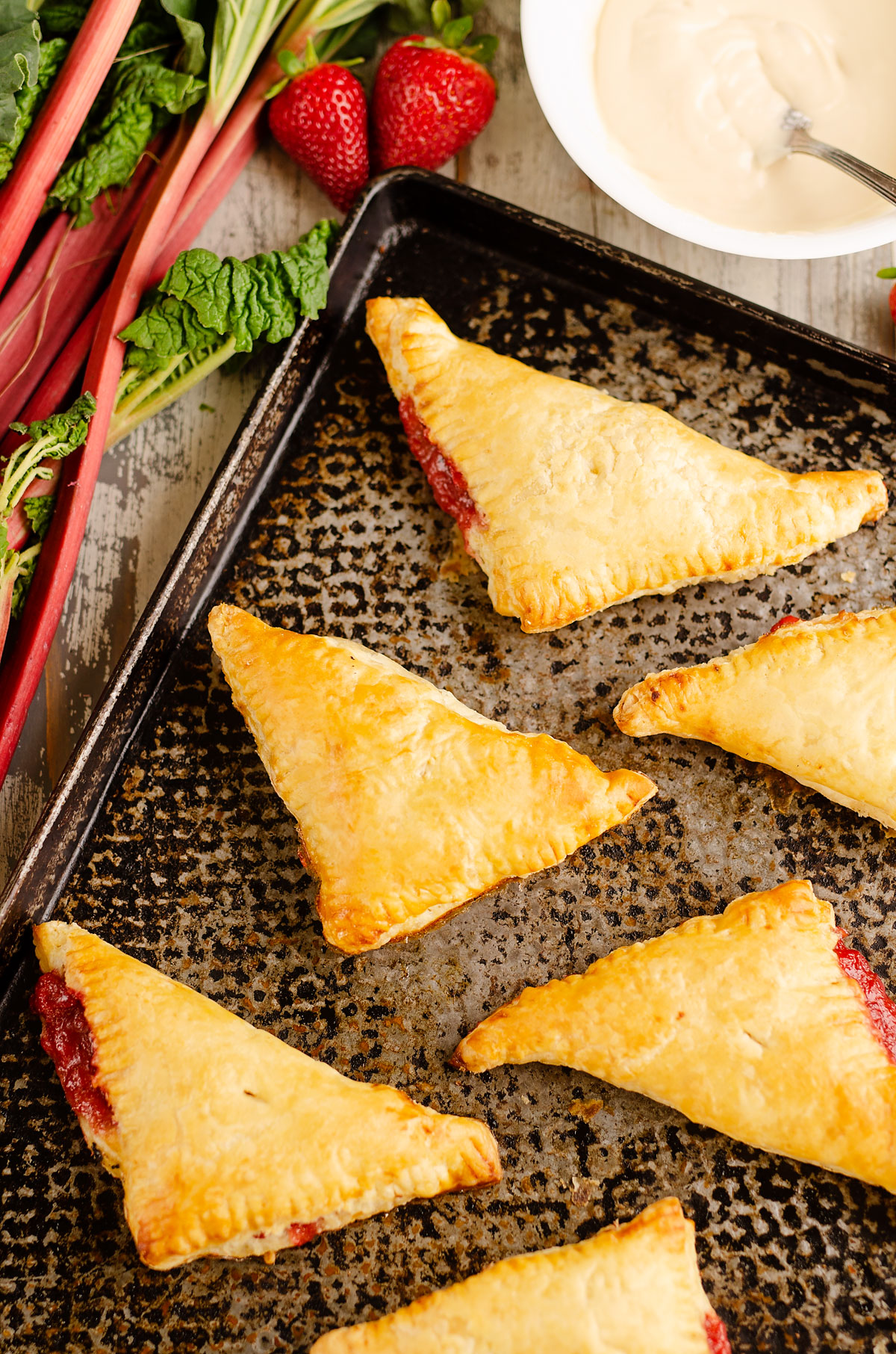 rhubarb turnovers on baking sheet with bowl of frosting