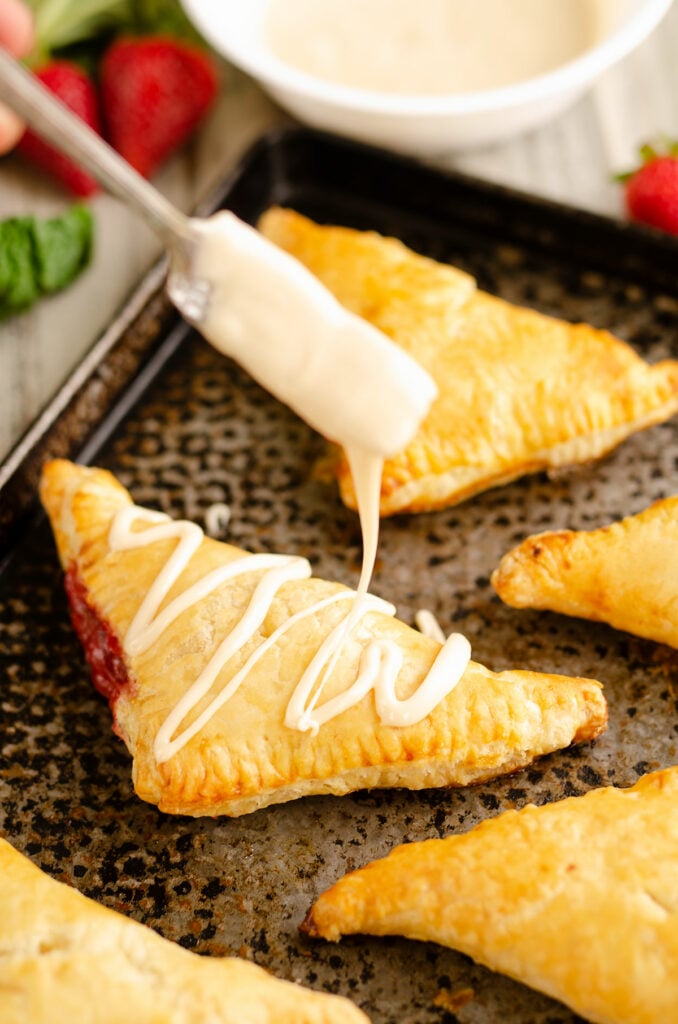vanilla frosting drizzled over rhubarb turnovers on pan
