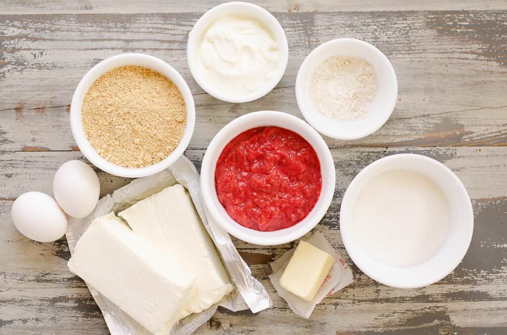 ingredients for strawberry rhubarb mini cheesecakes in bowls on table