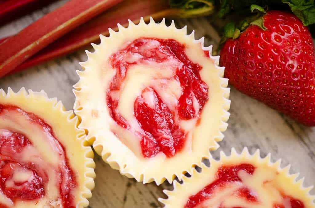 swirled strawberry rhubarb mini cheesecakes on table