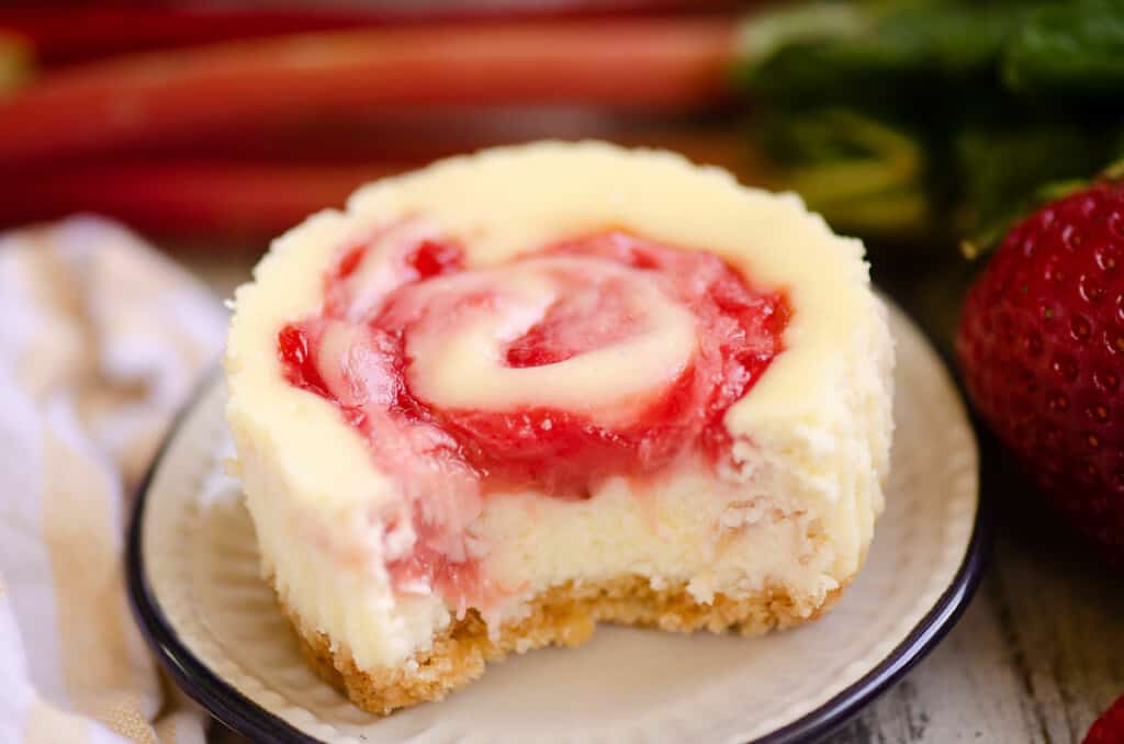 bite out of strawberry rhubarb mini cheesecake on small plate