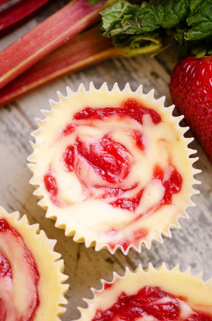 swirled strawberry rhubarb mini cheesecakes on table