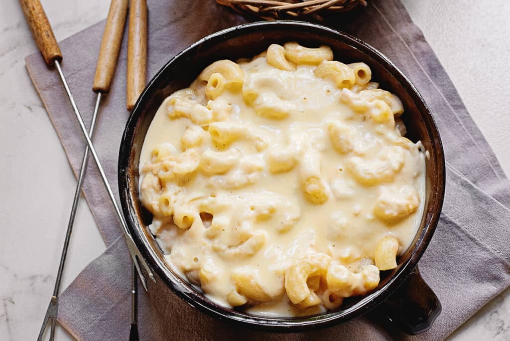 creamy macaroni and cheese fondue on pot on table with fondue forks and napkin