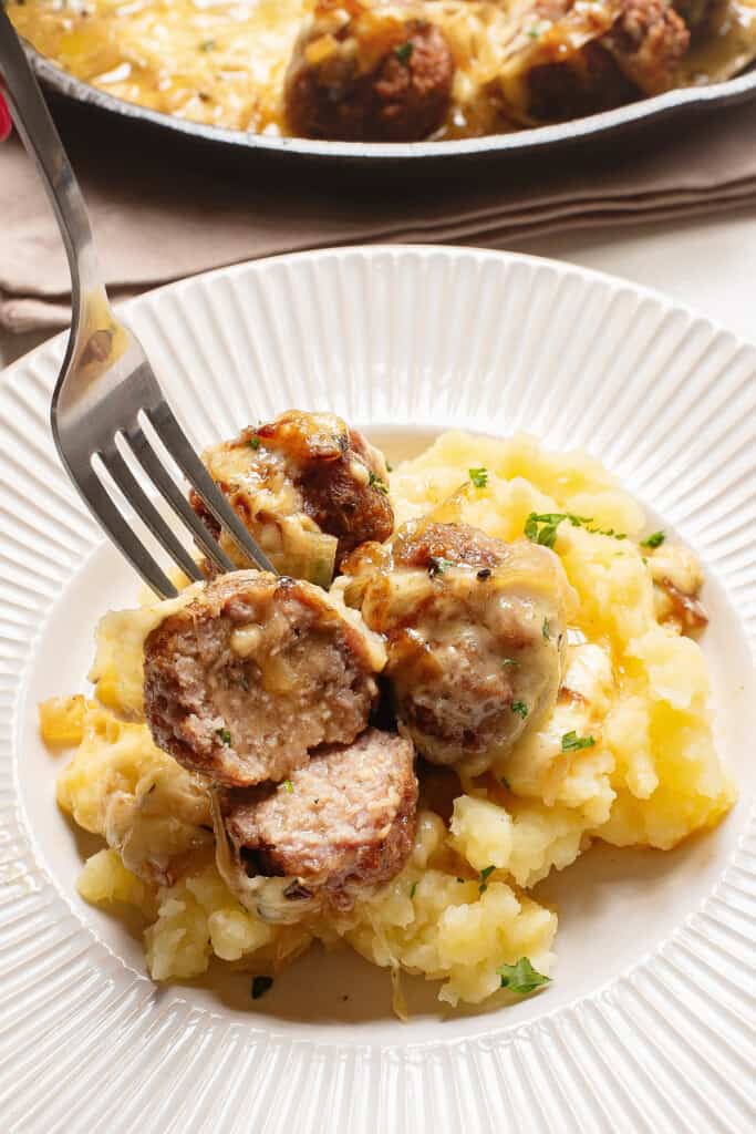 sliced French onion meatballs over mashed potatoes with fork