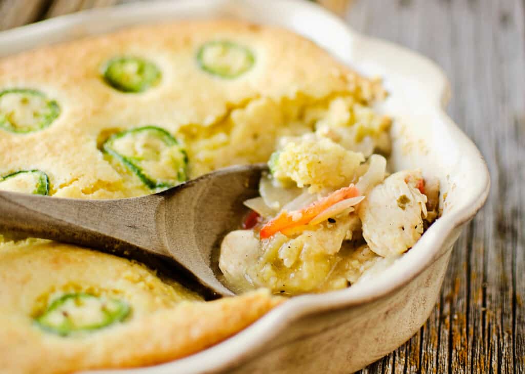 Jalapeno topped cornbread and chicken casserole in pan on rustic table