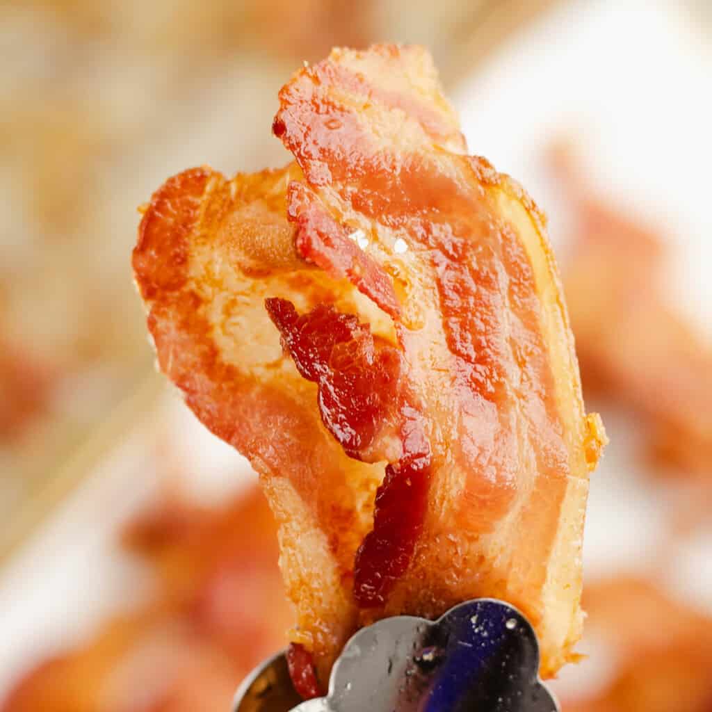 baked bacon in tongs