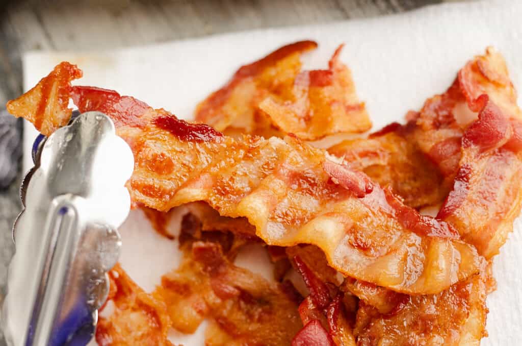 baked bacon on paper towel with tongs