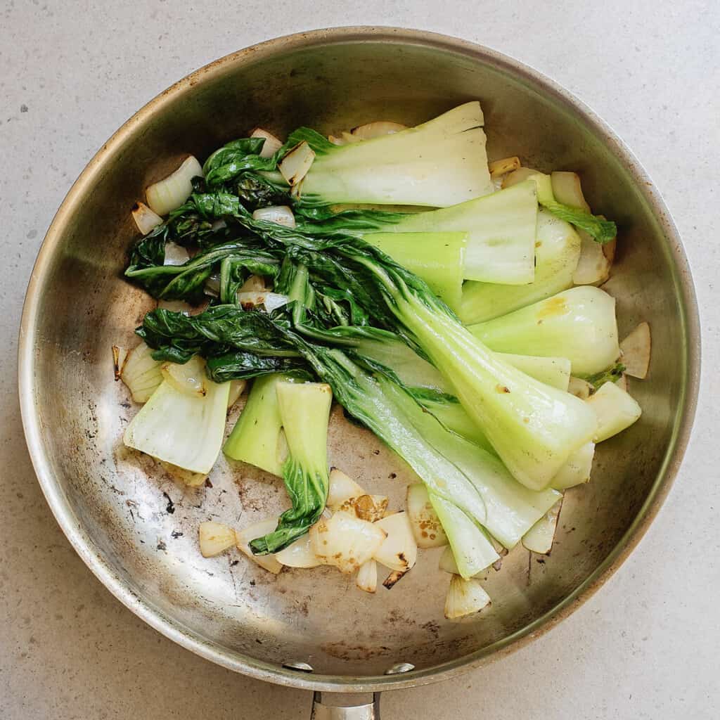 Bok choy and onions sautéed in pan