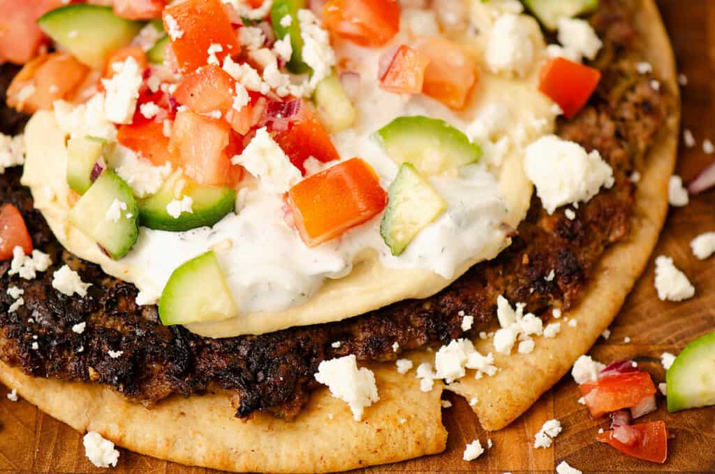 pita with smashed lamb and topped with hummus, tzatziki and cucumber and tomato salad