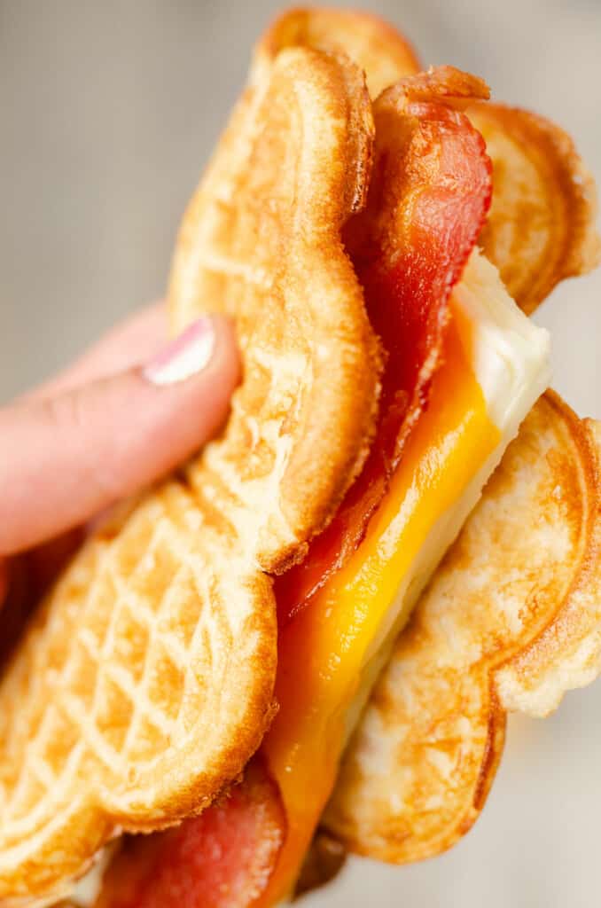 cheesy egg and bacon breakfast waffle sandwich in hand